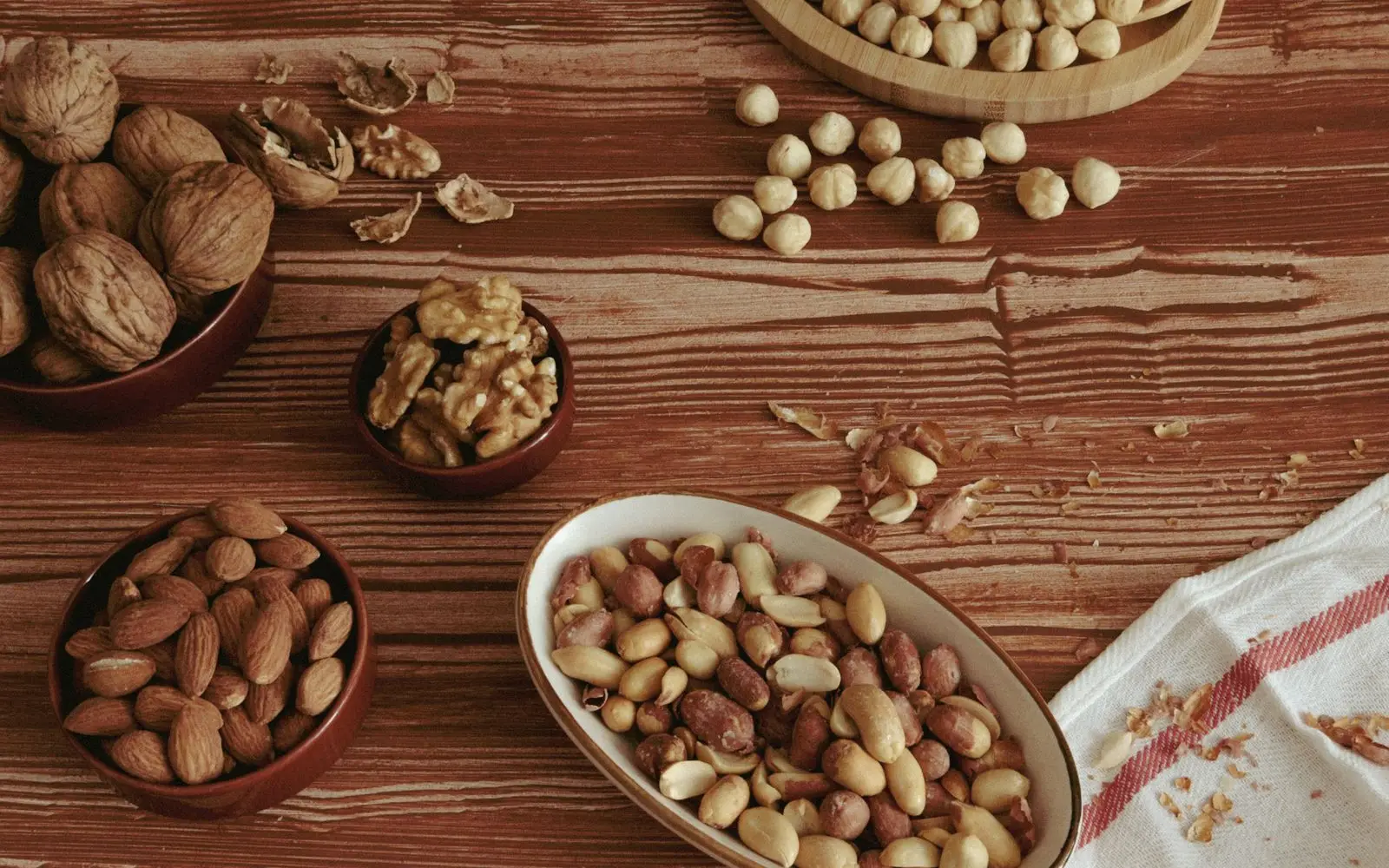 Bowls of peanuts, almonds, walnuts and hazelnuts on a wooden table