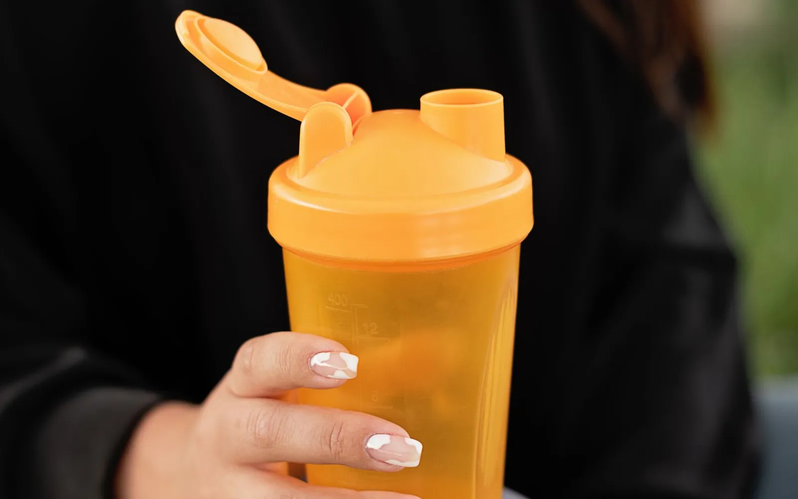 A hand holding an orange plastic shaker bottle with its flip lid open, in front of a black jumper