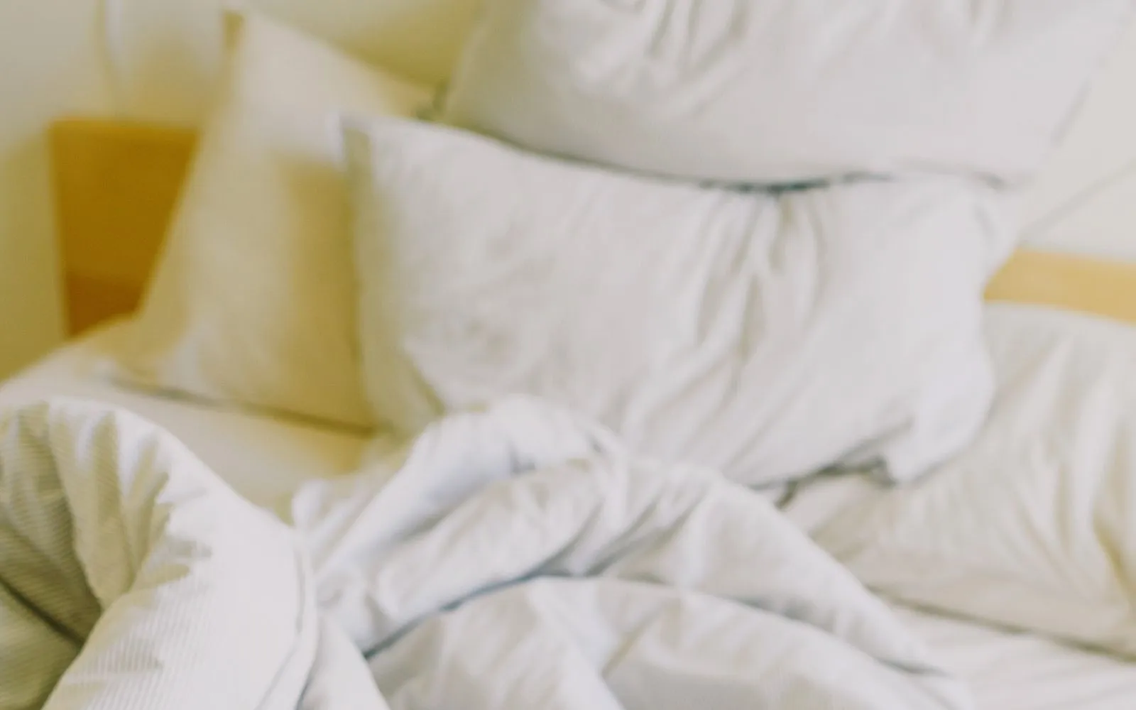 An unmade bed with white pillows and a crumpled grey-striped duvet in daylight.