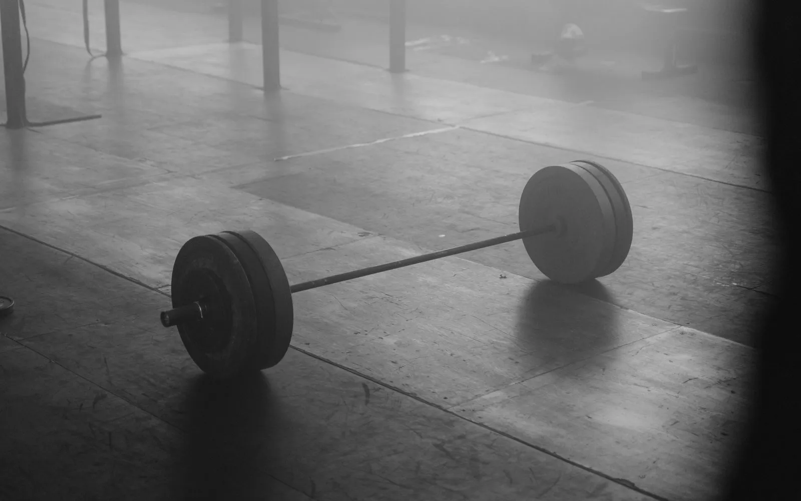 A loaded barbell resting on an empty gym floor, in black and white