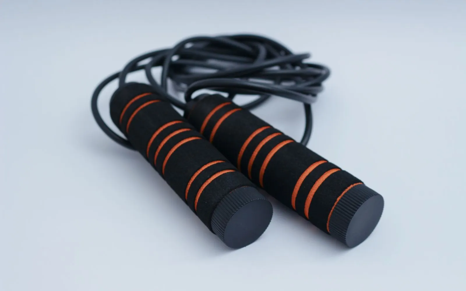 A black skipping rope with foam handles, coiled on a plain pale surface.