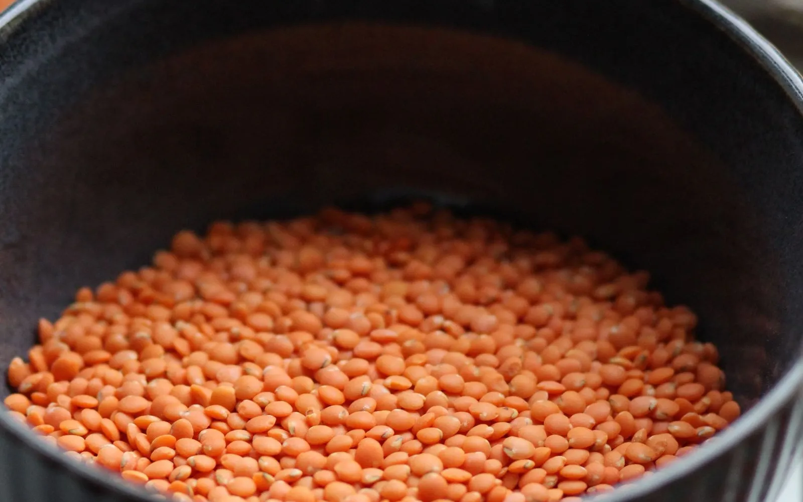 Dry red lentils in a dark bowl, with brown eggs in a carton behind