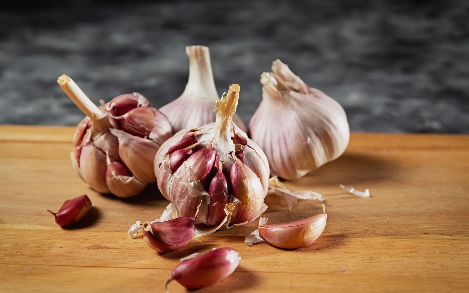 Whole garlic bulbs and loose cloves on a wooden chopping board.