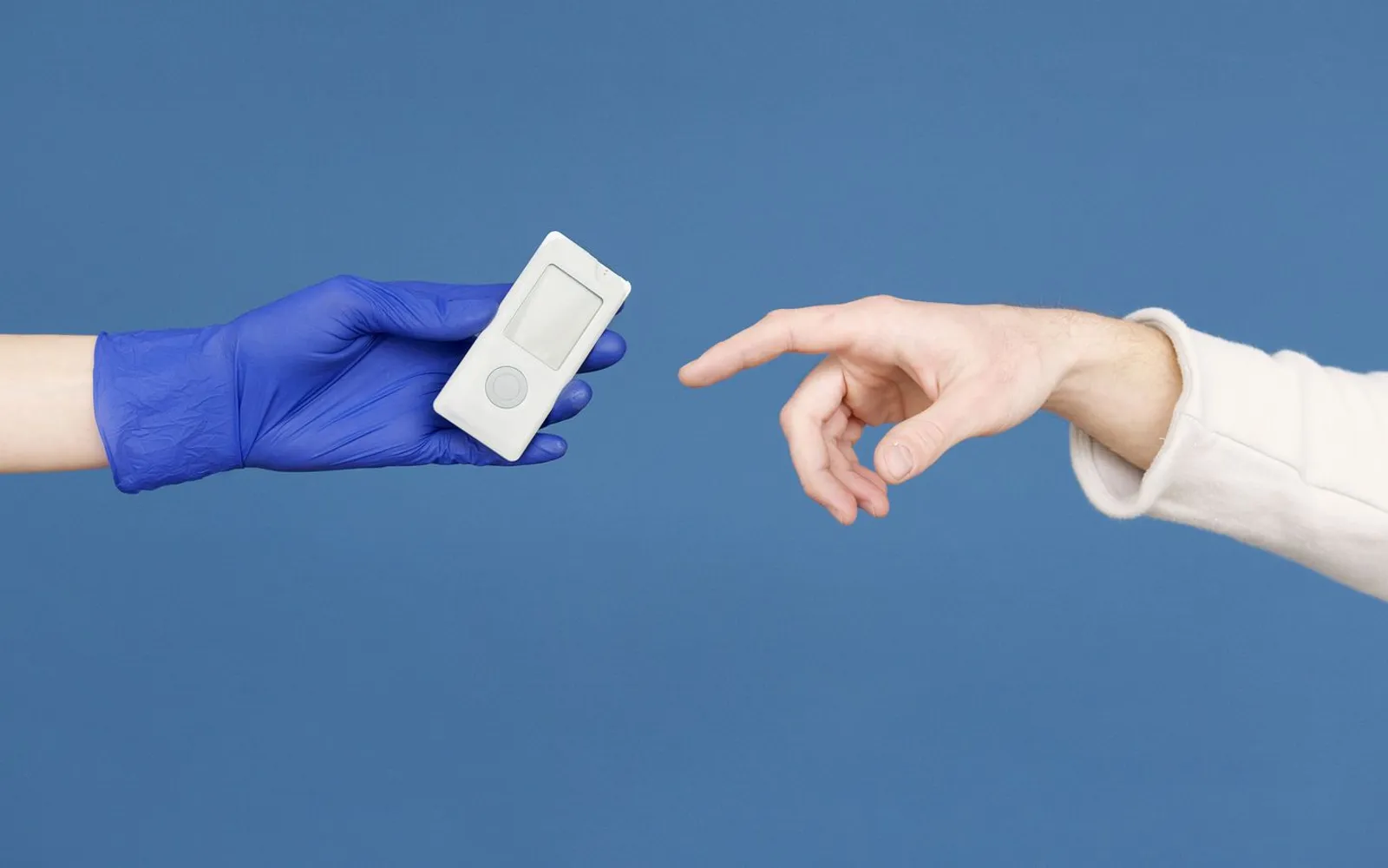 A gloved hand holds out a plain white blood glucose meter towards another hand on a blue background