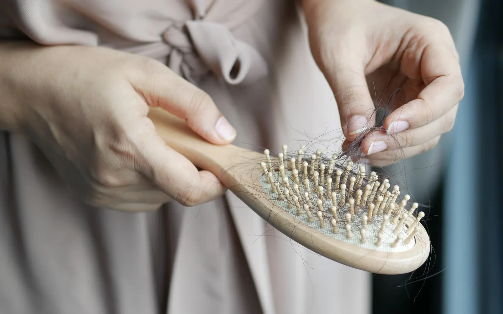 Two hands pulling loose strands of hair from a wooden hairbrush