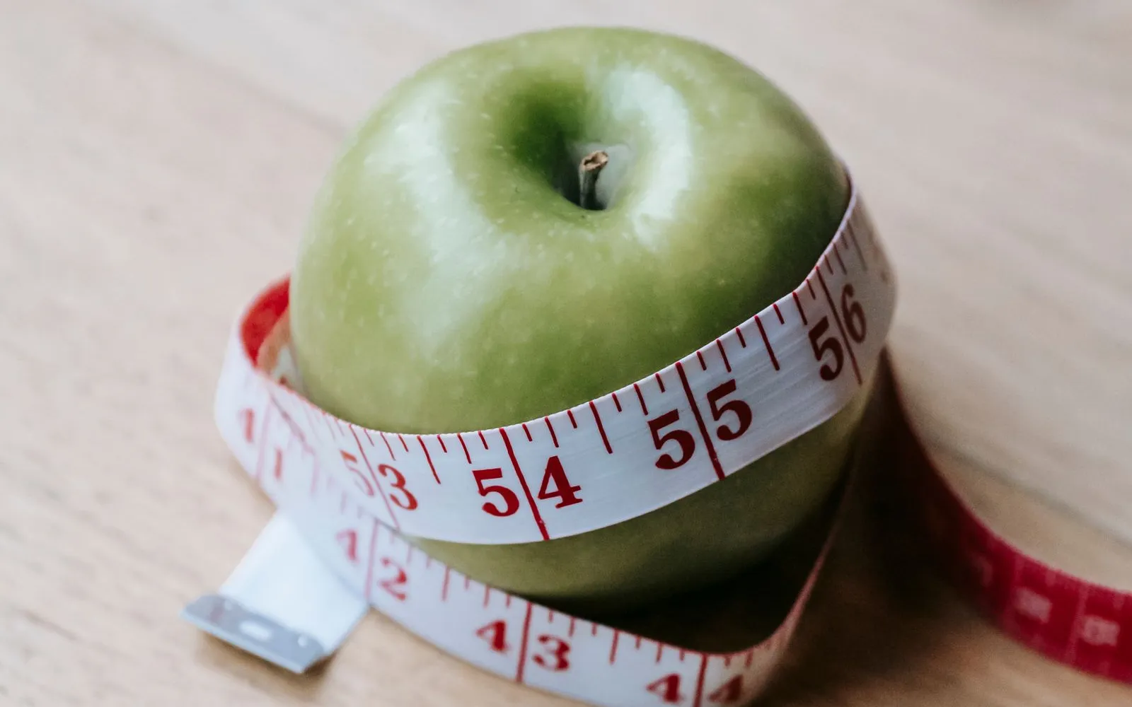A green apple with a tape measure wrapped around it on a wooden table