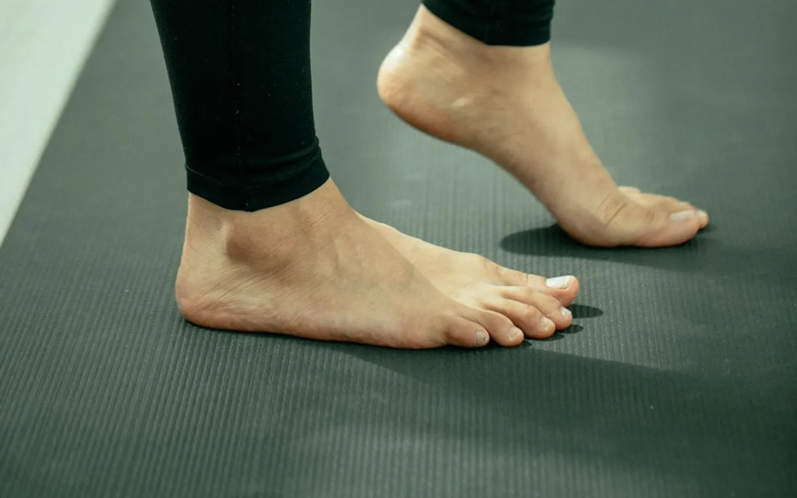 Legs in black leggings on an exercise mat, one bare heel lifted off the floor