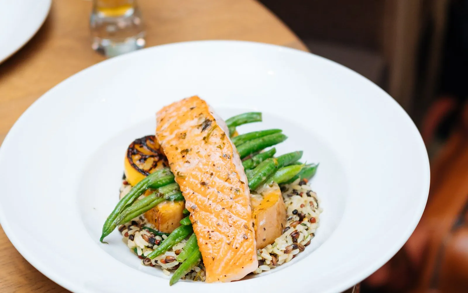 A fillet of salmon on green beans and wholegrain rice in a white bowl on a wooden table