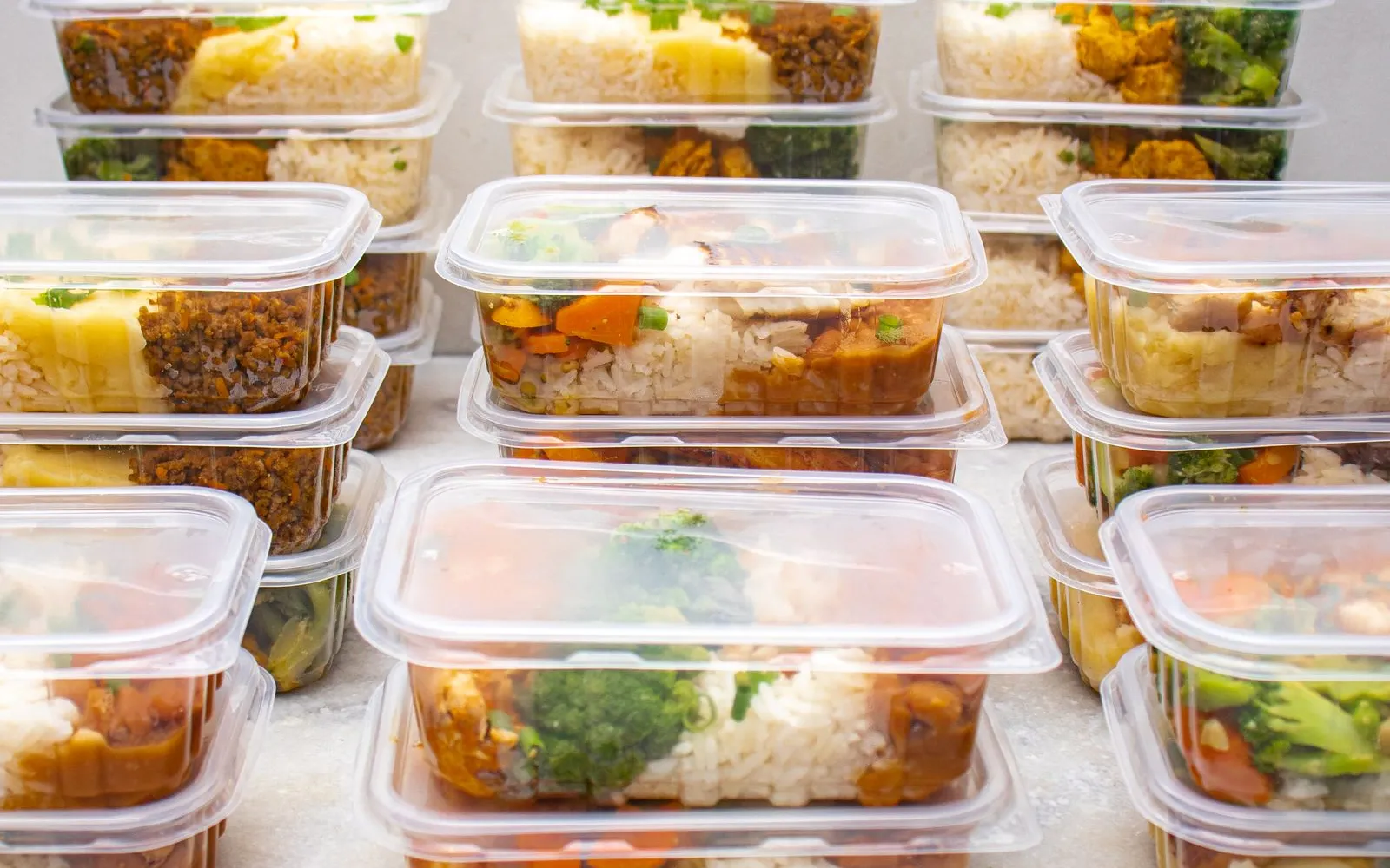 Stacks of clear plastic meal prep boxes filled with rice, vegetables, mince and chicken