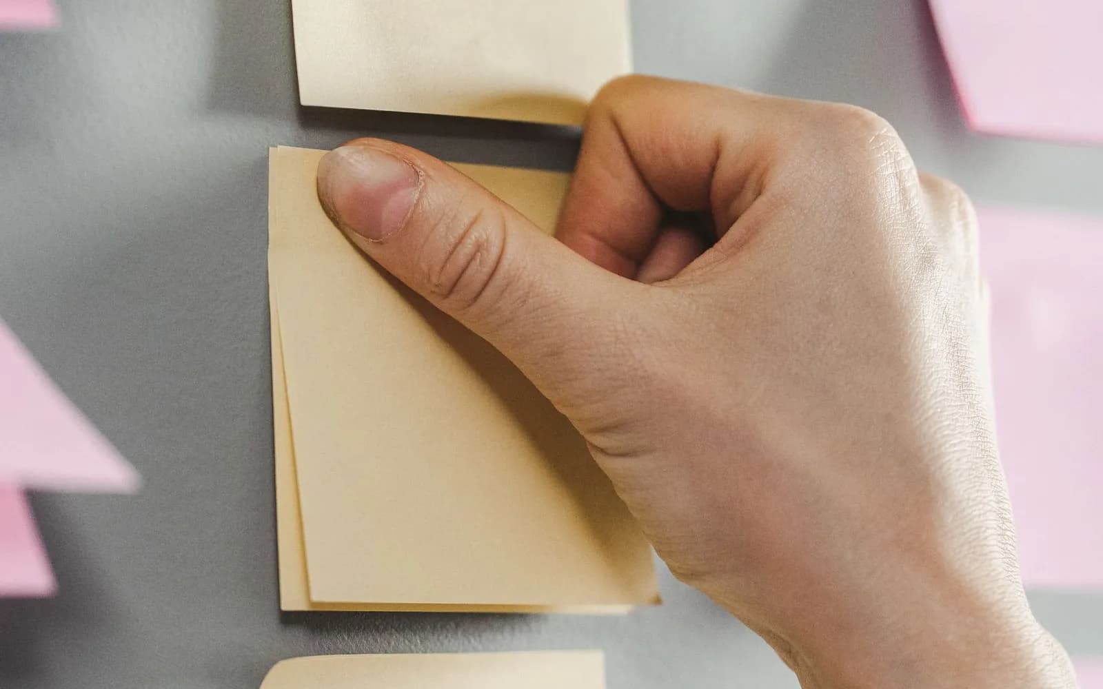 A hand pressing a blank yellow sticky note onto a grey wall among other blank notes