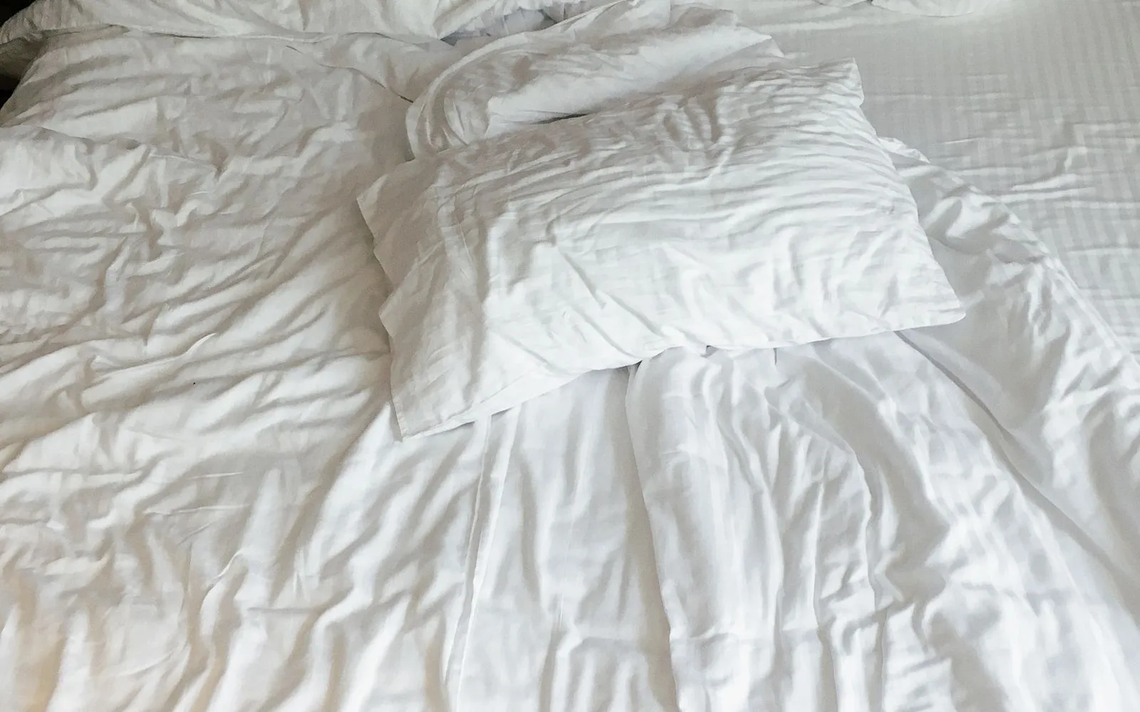 A rumpled white duvet and pillows on an unmade bed against a dark grey headboard