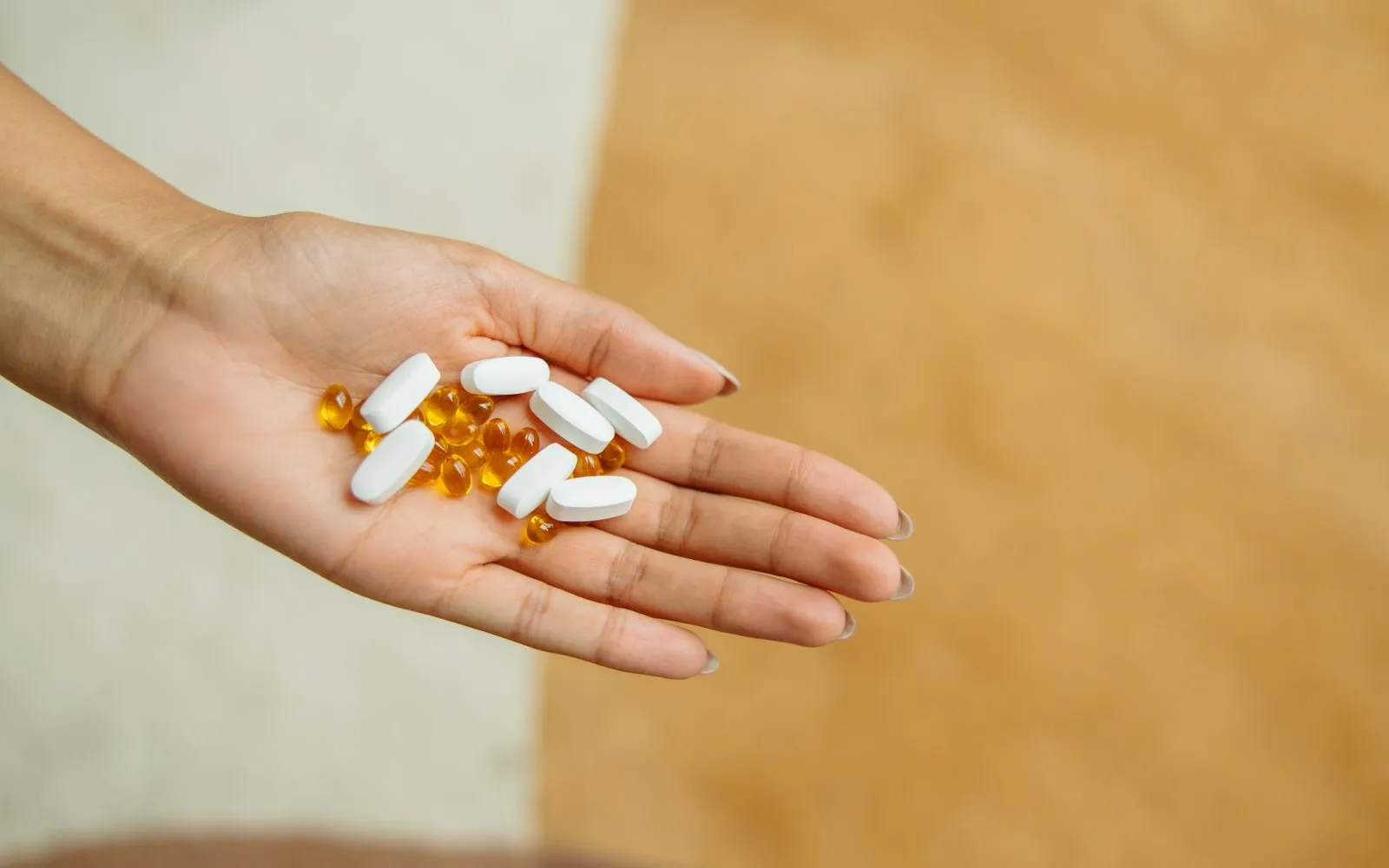 An open hand holding white tablets and small yellow softgel capsules
