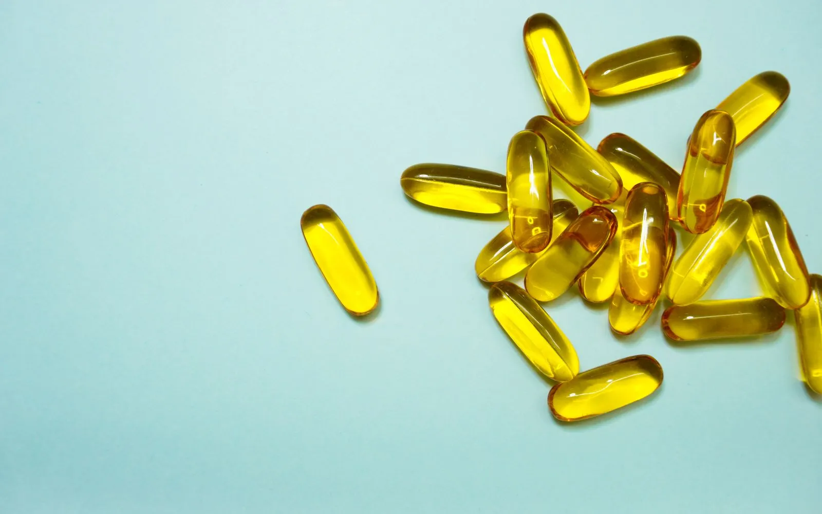 Yellow softgel oil capsules scattered on a pale blue surface