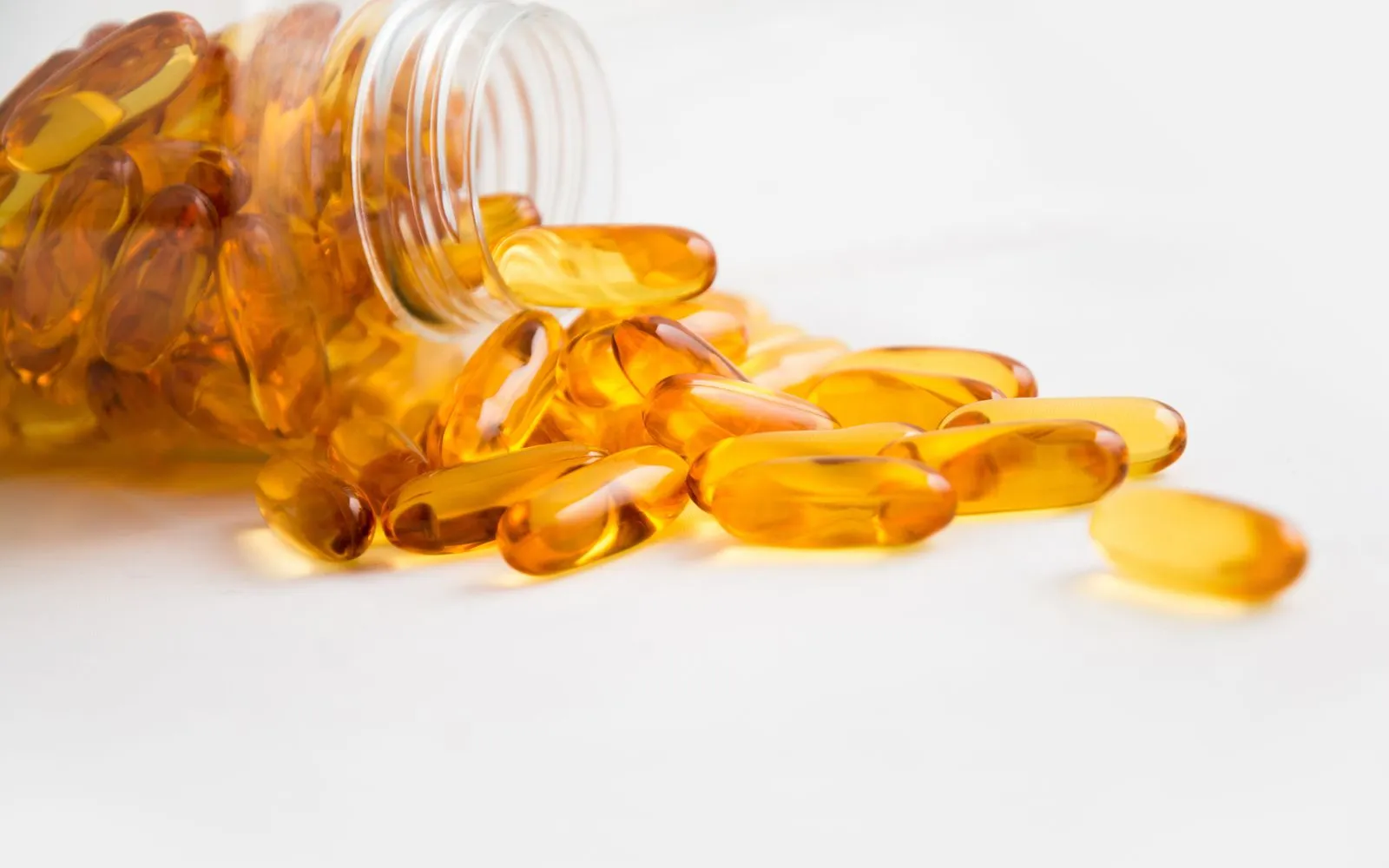 Golden fish oil softgel capsules spilling from a clear bottle onto a white surface.