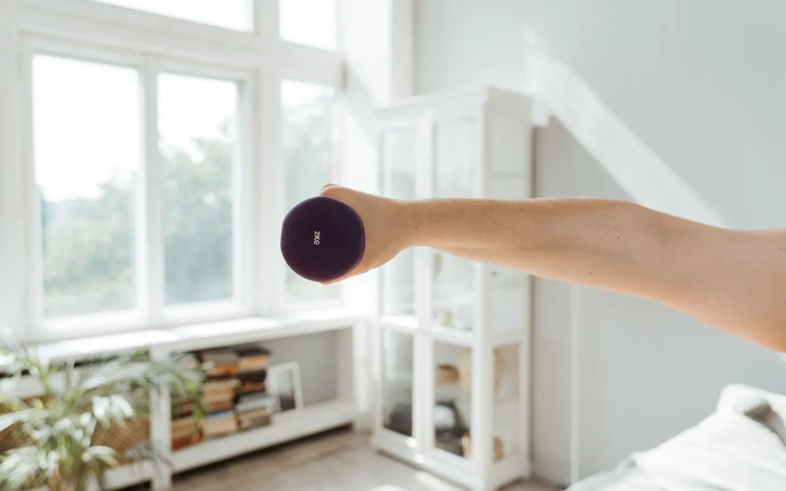An outstretched arm holding a small purple dumbbell in a bright living room.