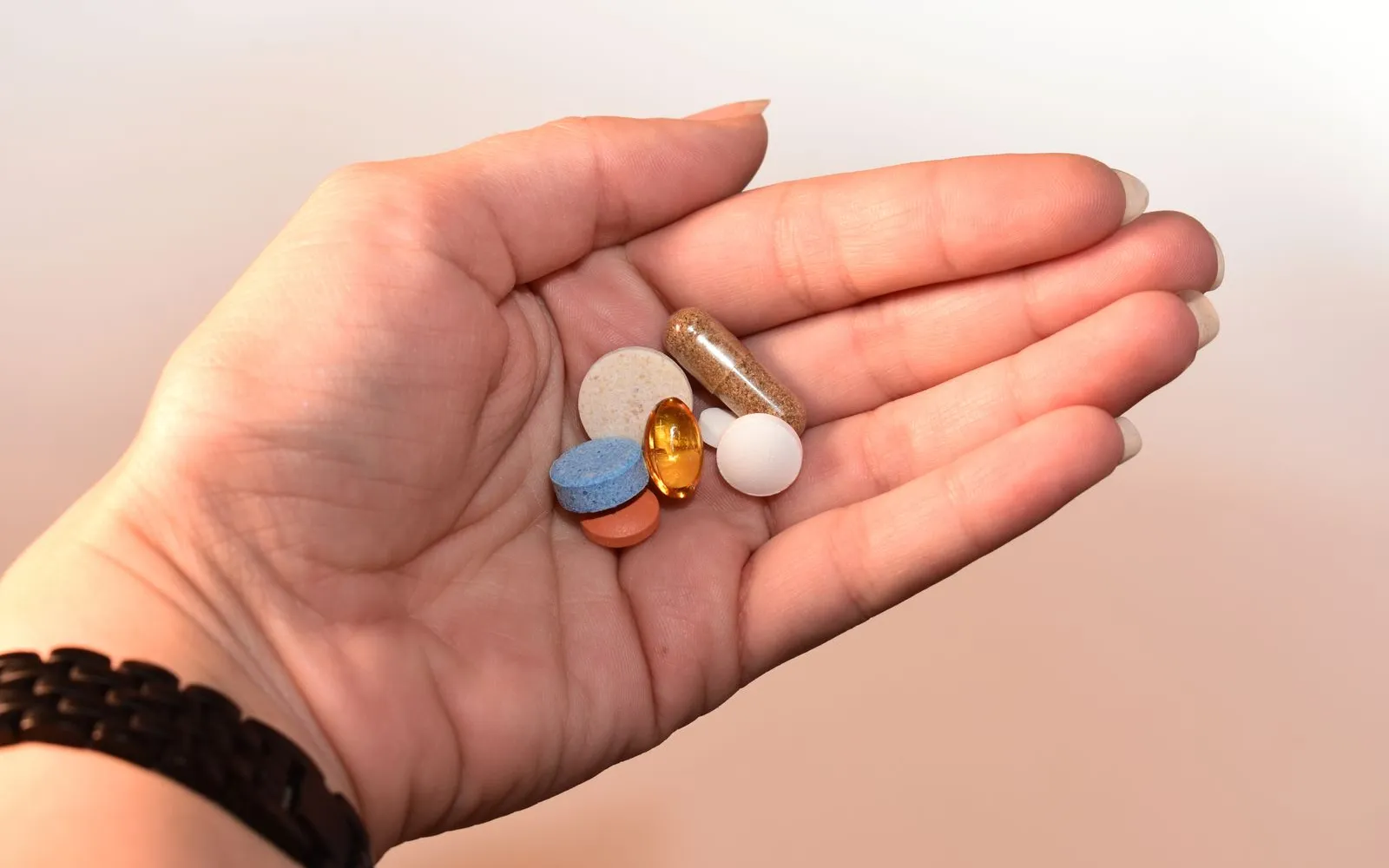 An open hand holding a few assorted supplement tablets, a capsule and a golden softgel