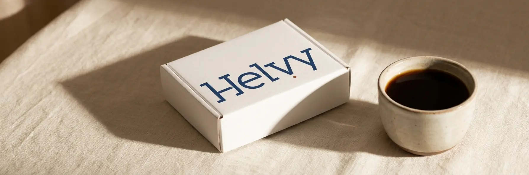 The Helvy blood test kit box on warm ivory linen beside a cup of coffee in morning light.